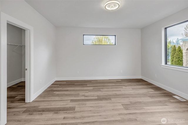 unfurnished bedroom featuring a walk in closet, light wood-type flooring, and visible vents