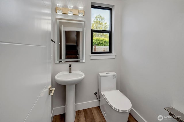 half bath with toilet, baseboards, a sink, and wood finished floors