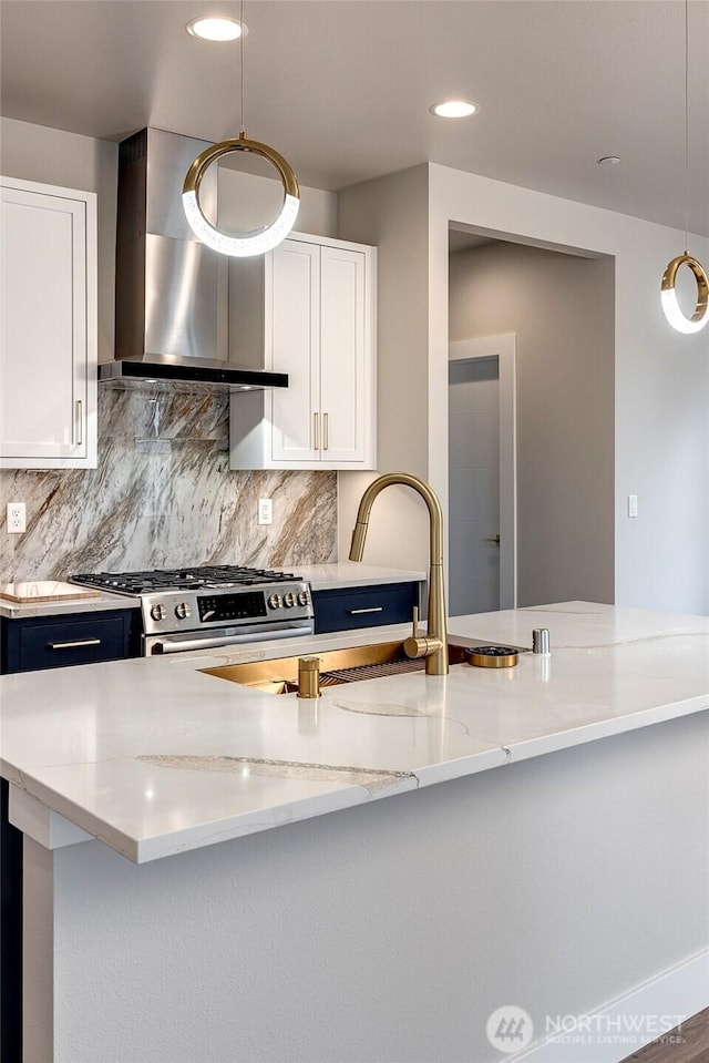 kitchen with blue cabinets, light stone countertops, stainless steel gas stove, white cabinetry, and wall chimney exhaust hood
