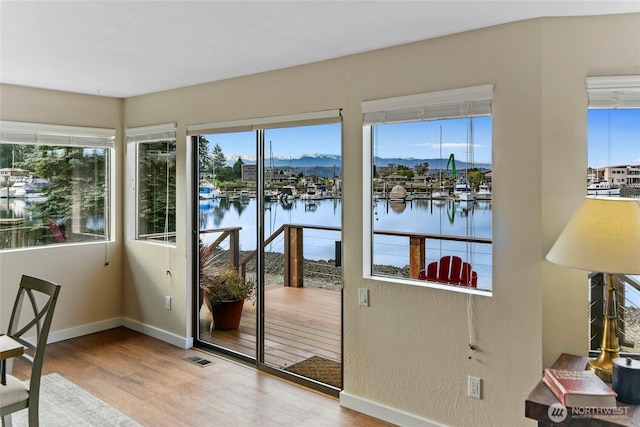 doorway to outside featuring visible vents, a water view, baseboards, and wood finished floors