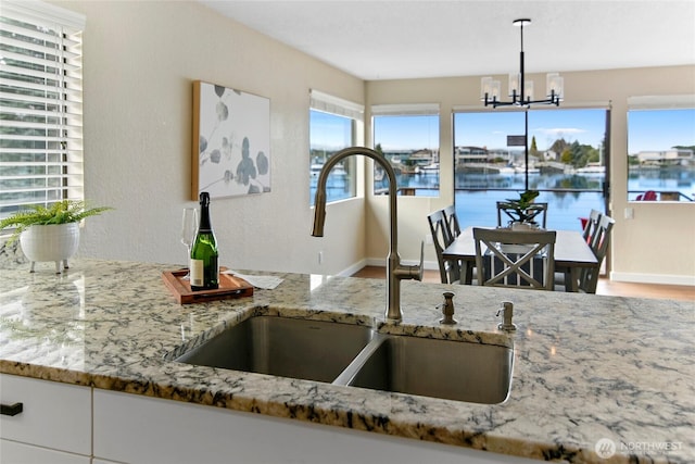 kitchen with a sink, decorative light fixtures, light stone counters, white cabinets, and baseboards