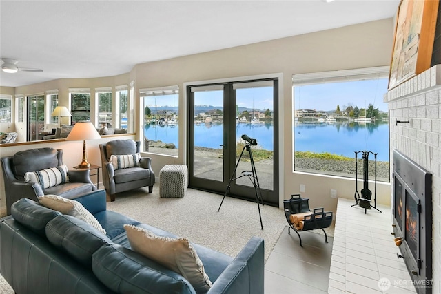 sunroom featuring a glass covered fireplace, a ceiling fan, and a water view