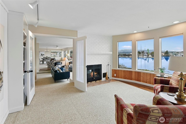 living room with recessed lighting, a water view, light colored carpet, and a fireplace