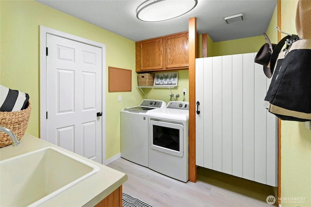 clothes washing area featuring visible vents, washer and clothes dryer, light wood-style floors, cabinet space, and a sink