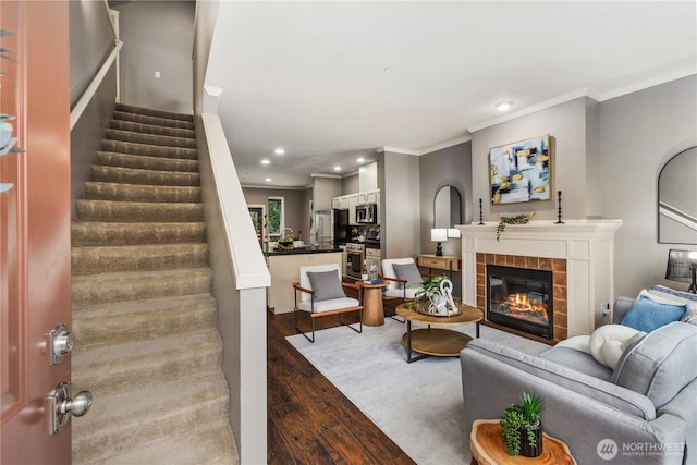 living area featuring a tile fireplace, ornamental molding, wood finished floors, stairs, and recessed lighting