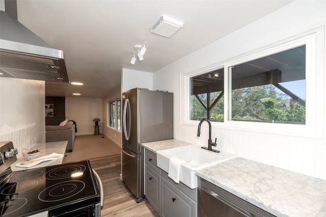 kitchen featuring light stone countertops, light wood finished floors, stainless steel appliances, and a sink