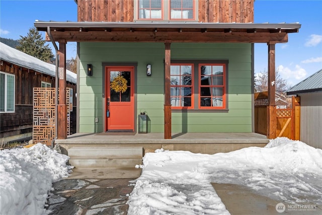 snow covered property entrance featuring board and batten siding and covered porch