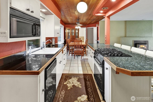 kitchen with a fireplace, a breakfast bar area, white cabinets, a sink, and black appliances