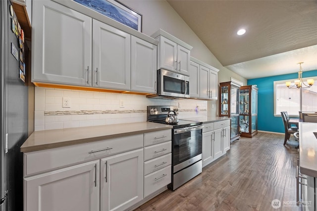 kitchen with pendant lighting, stainless steel appliances, lofted ceiling, decorative backsplash, and white cabinetry