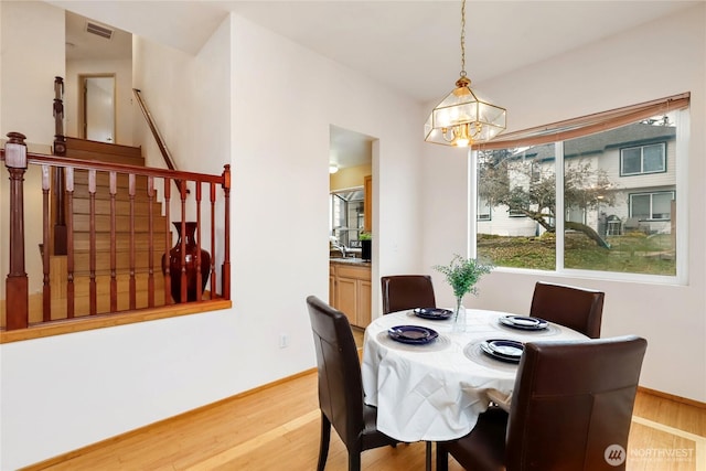 dining room featuring light wood-type flooring, stairway, baseboards, and visible vents