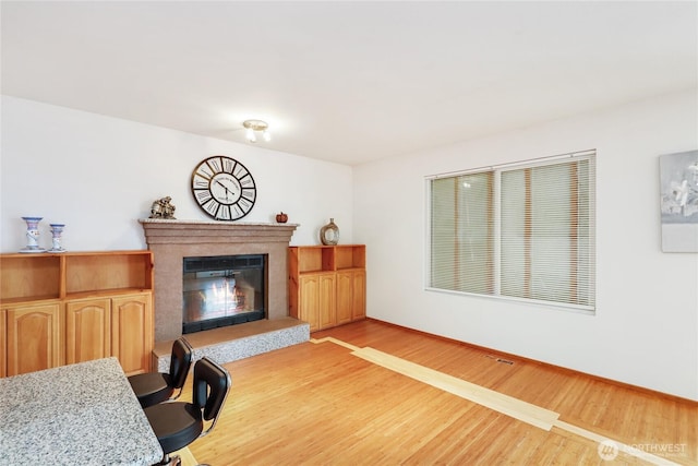 living area with light wood-style floors, baseboards, and a glass covered fireplace