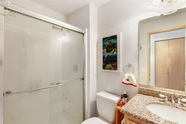 bathroom with toilet, a stall shower, a textured wall, and vanity