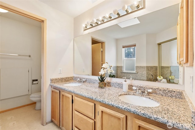 bathroom with double vanity, a skylight, a sink, and toilet