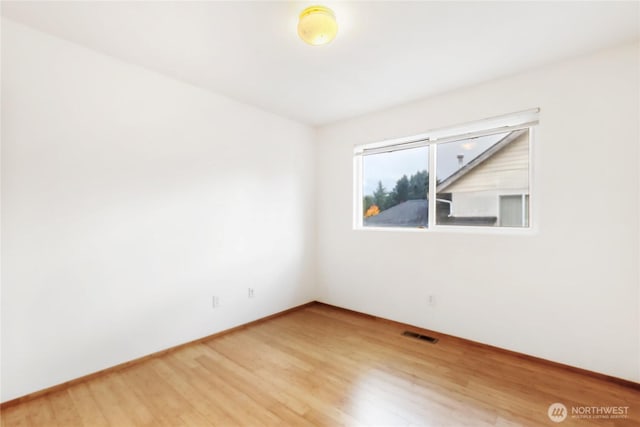 empty room featuring wood finished floors, visible vents, and baseboards