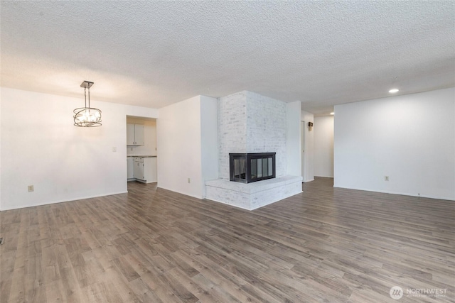 unfurnished living room featuring a textured ceiling, a chandelier, wood finished floors, and a multi sided fireplace