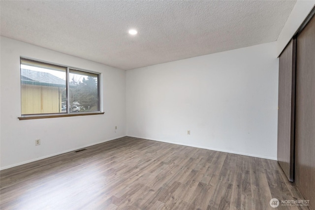 unfurnished bedroom featuring a closet, visible vents, a textured ceiling, and wood finished floors