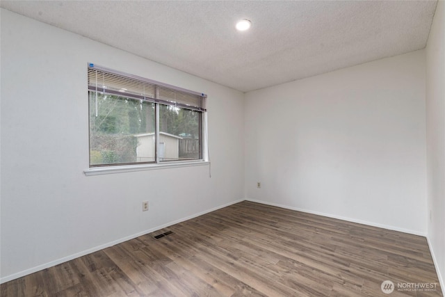 empty room featuring a textured ceiling, baseboards, and wood finished floors