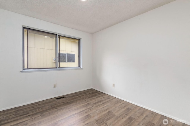 empty room with visible vents, a textured ceiling, baseboards, and wood finished floors