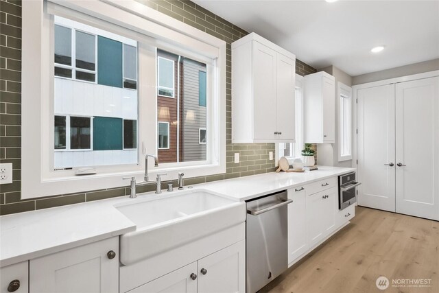 kitchen featuring light countertops, backsplash, appliances with stainless steel finishes, white cabinets, and a sink