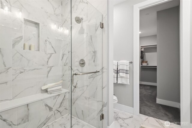 full bathroom with a walk in closet, marble finish floor, a marble finish shower, toilet, and baseboards