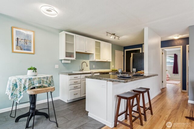 kitchen with refrigerator, a breakfast bar, glass insert cabinets, white cabinetry, and a peninsula