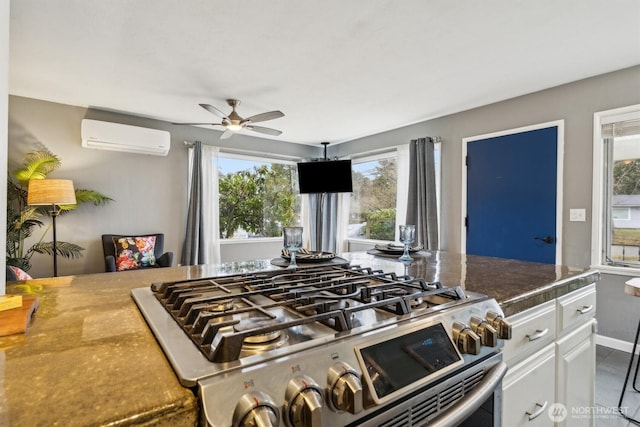 kitchen featuring dark countertops, a ceiling fan, an AC wall unit, white cabinets, and gas range