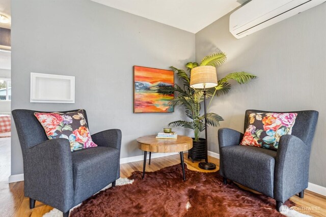 living area featuring baseboards, wood finished floors, and a wall mounted AC