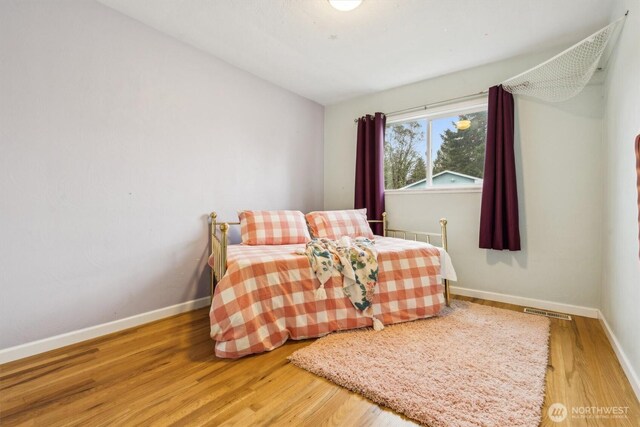 bedroom with wood finished floors, visible vents, and baseboards