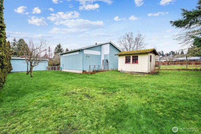 back of house featuring a shed, fence, a lawn, and an outbuilding