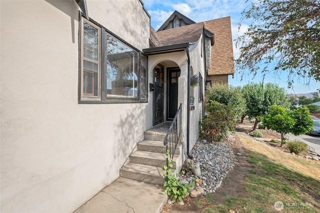 entrance to property featuring roof with shingles and stucco siding