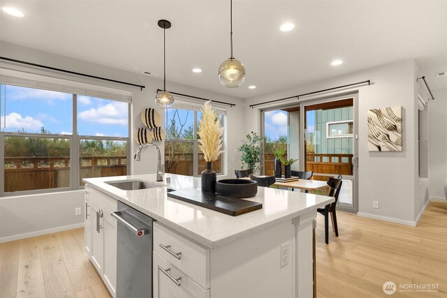 kitchen featuring light stone counters, a kitchen island with sink, white cabinets, a sink, and dishwasher