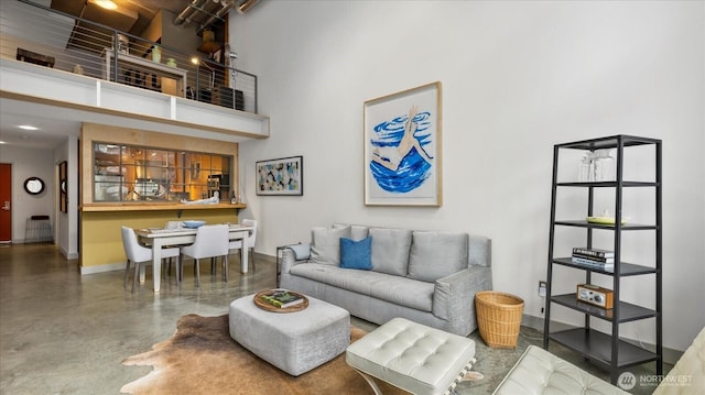 living area with finished concrete flooring, a towering ceiling, and baseboards