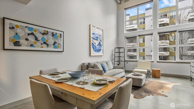 dining room featuring finished concrete floors, a towering ceiling, and baseboards