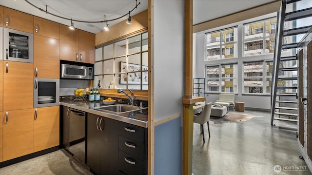 kitchen with stainless steel countertops, appliances with stainless steel finishes, a sink, concrete flooring, and track lighting