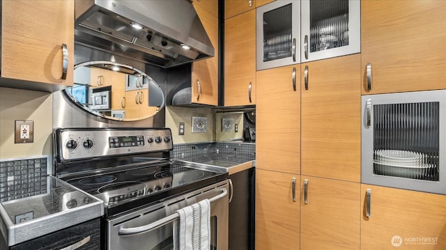 kitchen with glass insert cabinets, dark countertops, wall chimney range hood, and stainless steel electric stove