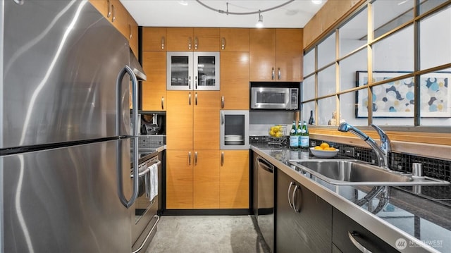 kitchen featuring brown cabinetry, dark countertops, appliances with stainless steel finishes, concrete flooring, and a sink