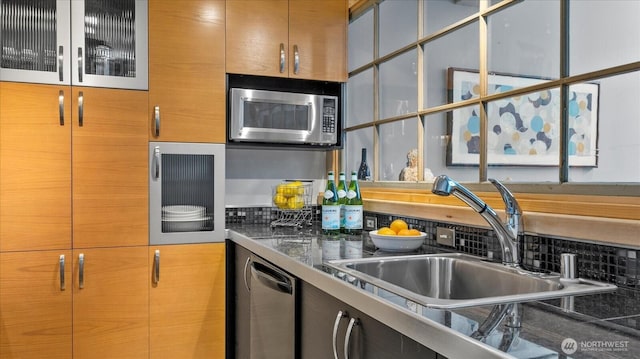 kitchen featuring dark countertops, glass insert cabinets, stainless steel appliances, and a sink