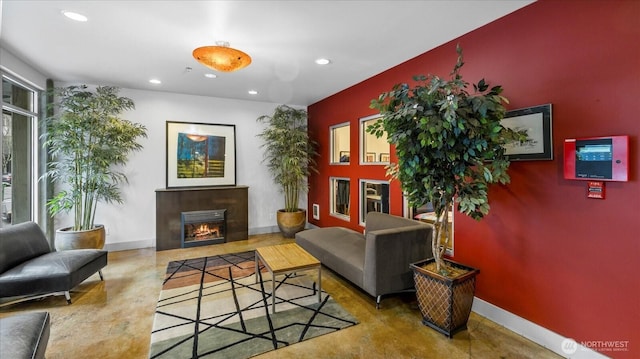 living area with concrete flooring, a glass covered fireplace, baseboards, and recessed lighting