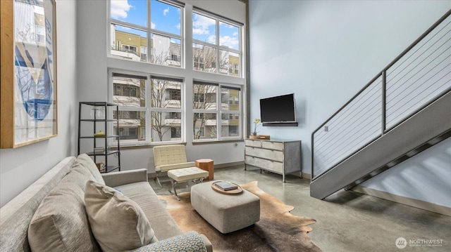 living area featuring stairway, concrete floors, a towering ceiling, and baseboards