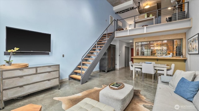 living room with finished concrete flooring, baseboards, a high ceiling, and stairway