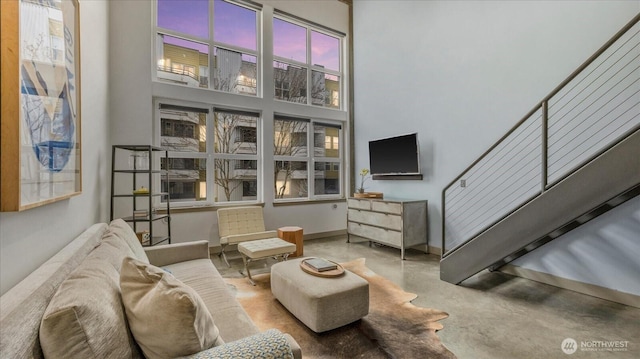 living area with baseboards, concrete floors, stairway, and a high ceiling