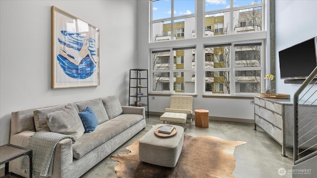 living room featuring finished concrete flooring, a high ceiling, and baseboards