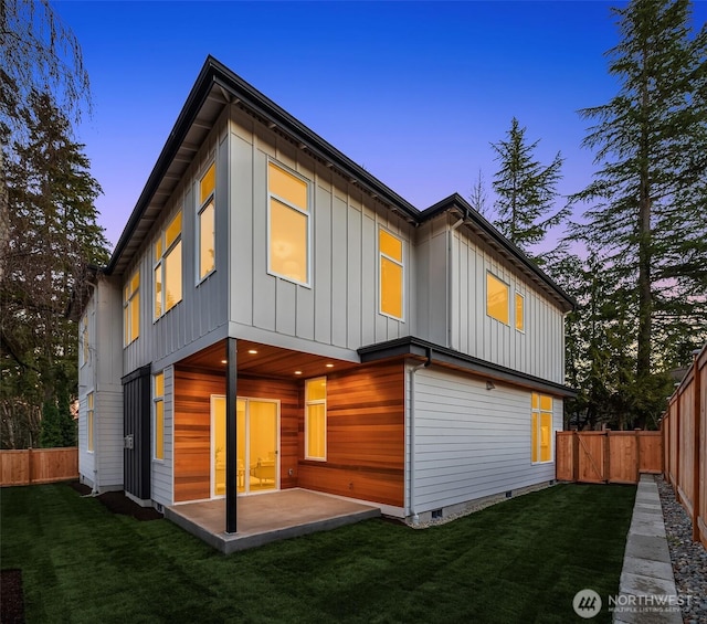 back of house at dusk with a yard, a fenced backyard, board and batten siding, and a patio