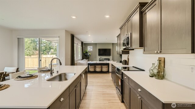 kitchen with a sink, light countertops, appliances with stainless steel finishes, dark brown cabinets, and a center island with sink