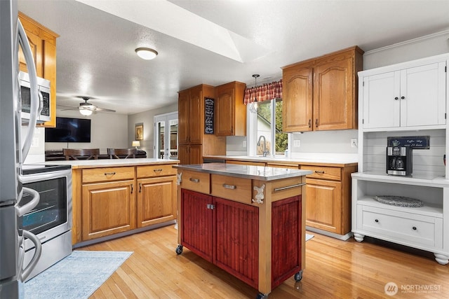 kitchen featuring ceiling fan, light wood-type flooring, brown cabinets, appliances with stainless steel finishes, and a sink