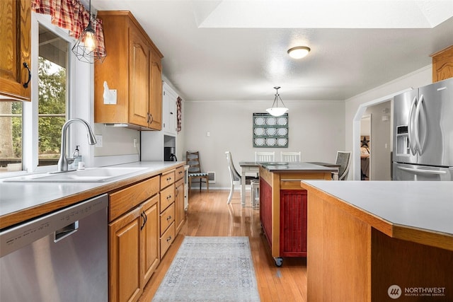 kitchen featuring pendant lighting, light wood-type flooring, brown cabinetry, stainless steel appliances, and a sink