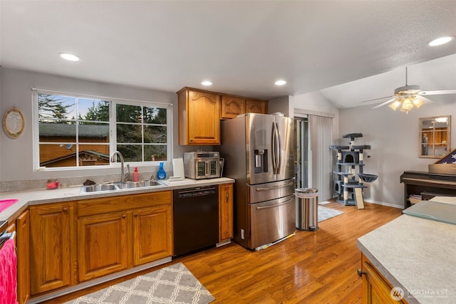 kitchen with stainless steel fridge, brown cabinetry, dishwasher, light countertops, and a sink