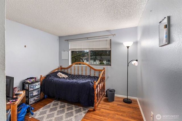 bedroom with a textured wall, a textured ceiling, baseboards, and wood finished floors