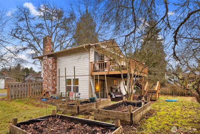 back of property featuring a vegetable garden, a chimney, a lawn, fence, and a deck