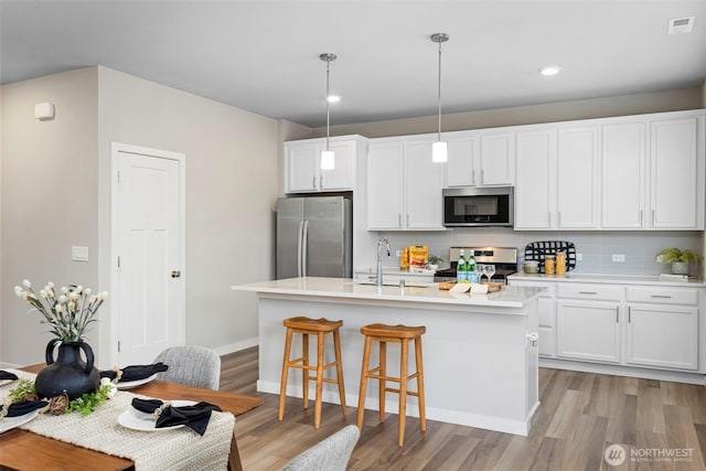 kitchen with stainless steel appliances, a sink, hanging light fixtures, light countertops, and an island with sink